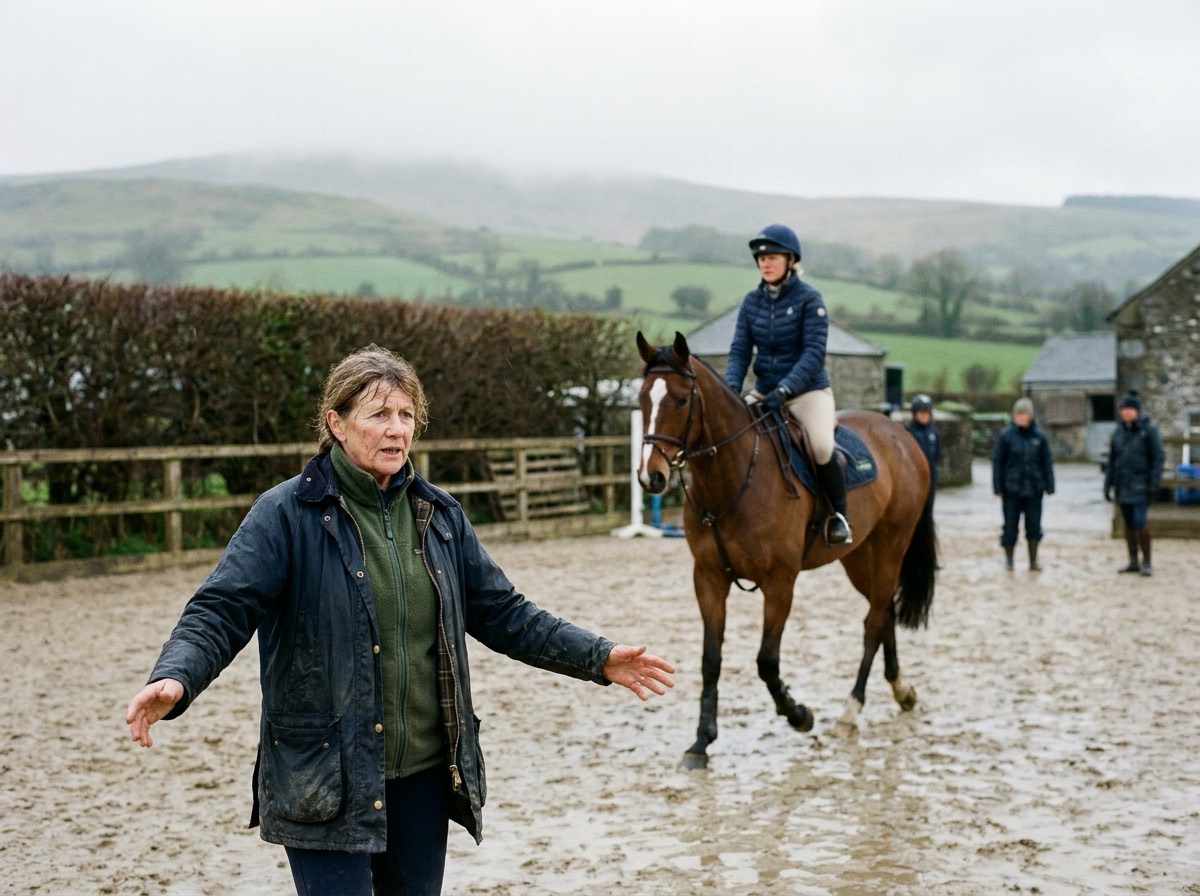 A coach on foot in the arena gives instruction as a rider trots her bay horse past